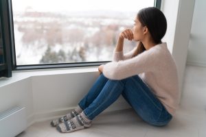 Depressed Young Girl Feeling Sad An Lonely, Anxious Looking Out The Window In Winter Unhappy Asian Woman Alone, Seasonal Depression At Home | See A Neurologist